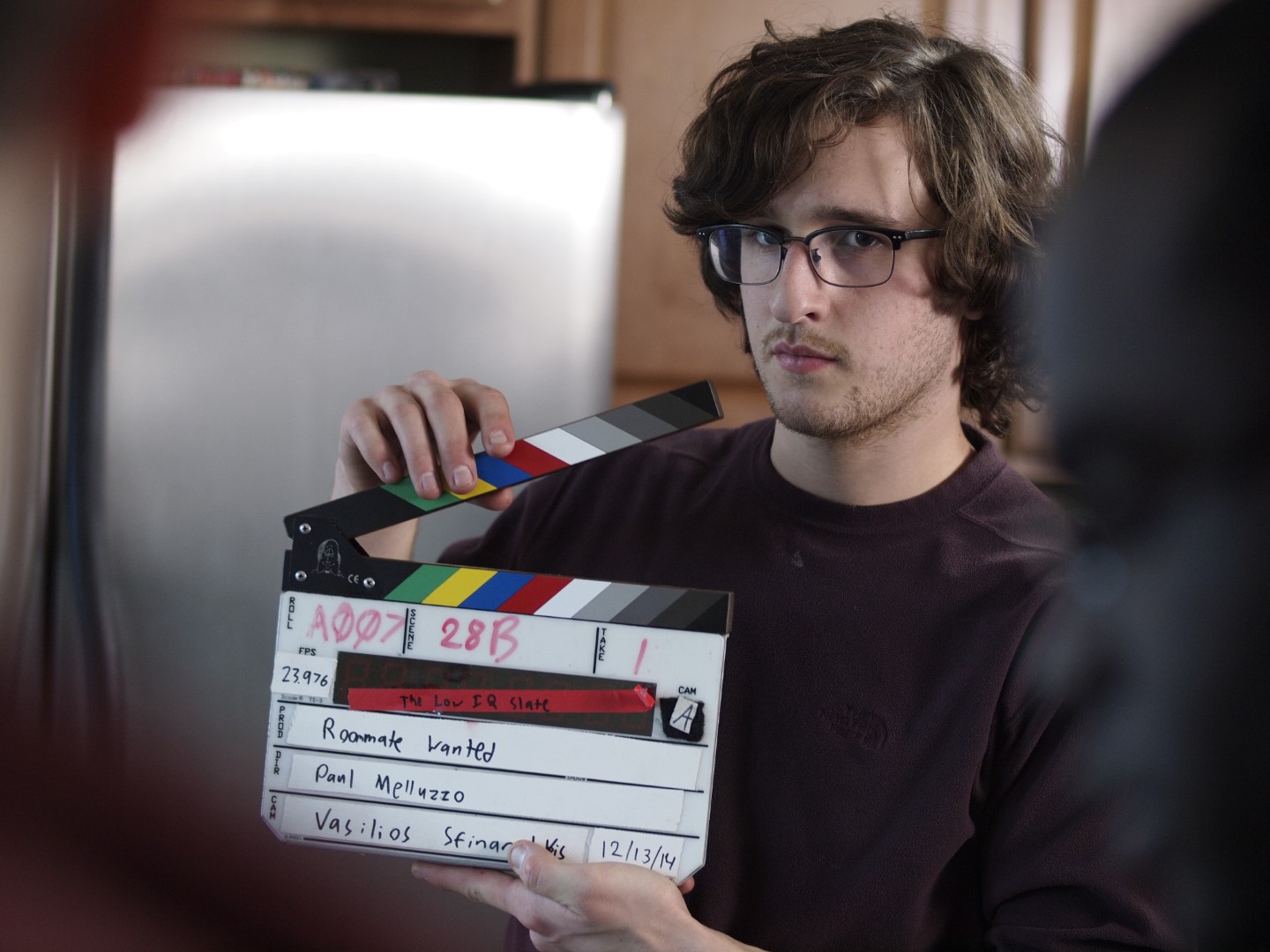 Young filmmaker holds a clapperboard on a film set, capturing the scene for a project titled 'Roommate Wanted.'