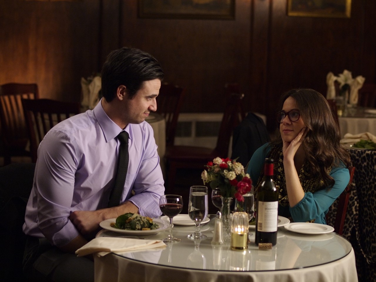 Couple enjoying a romantic dinner at a cozy restaurant, with wine and flowers on the table.