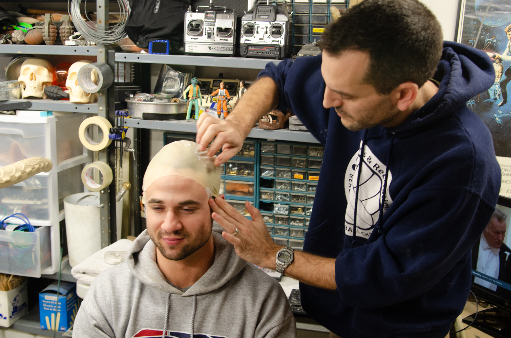 Artist applying a bald cap in a creative workshop with tools and props in the background.