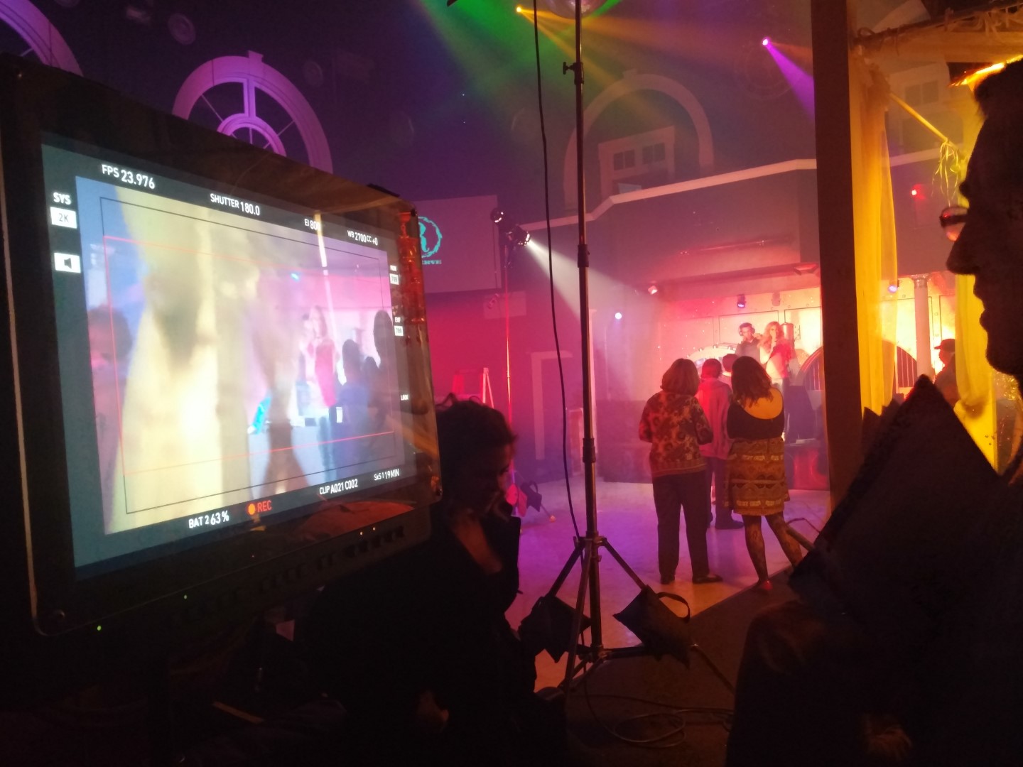 Behind-the-scenes of a vibrant music video shoot with colorful lights and crew preparing for recording.