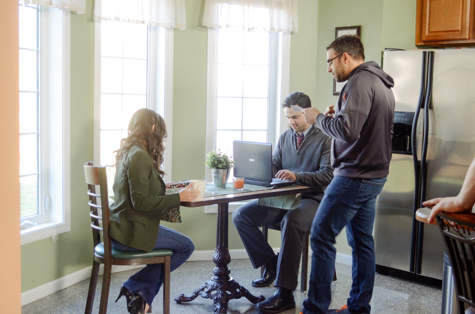 Three people collaborating in a bright kitchen with a laptop, coffee, and a cozy atmosphere.