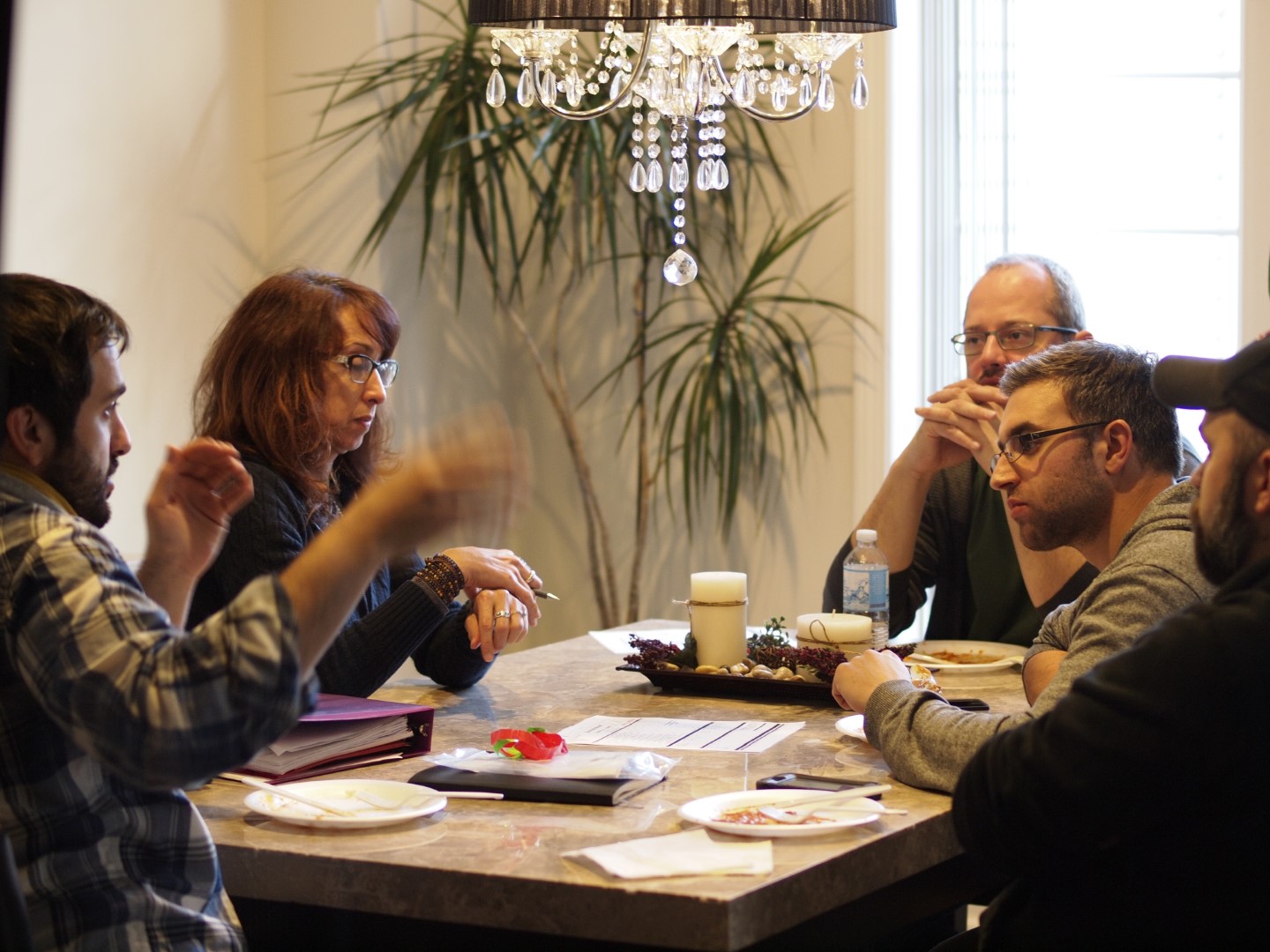Group of five people engaged in a discussion around a table with food and beverages.