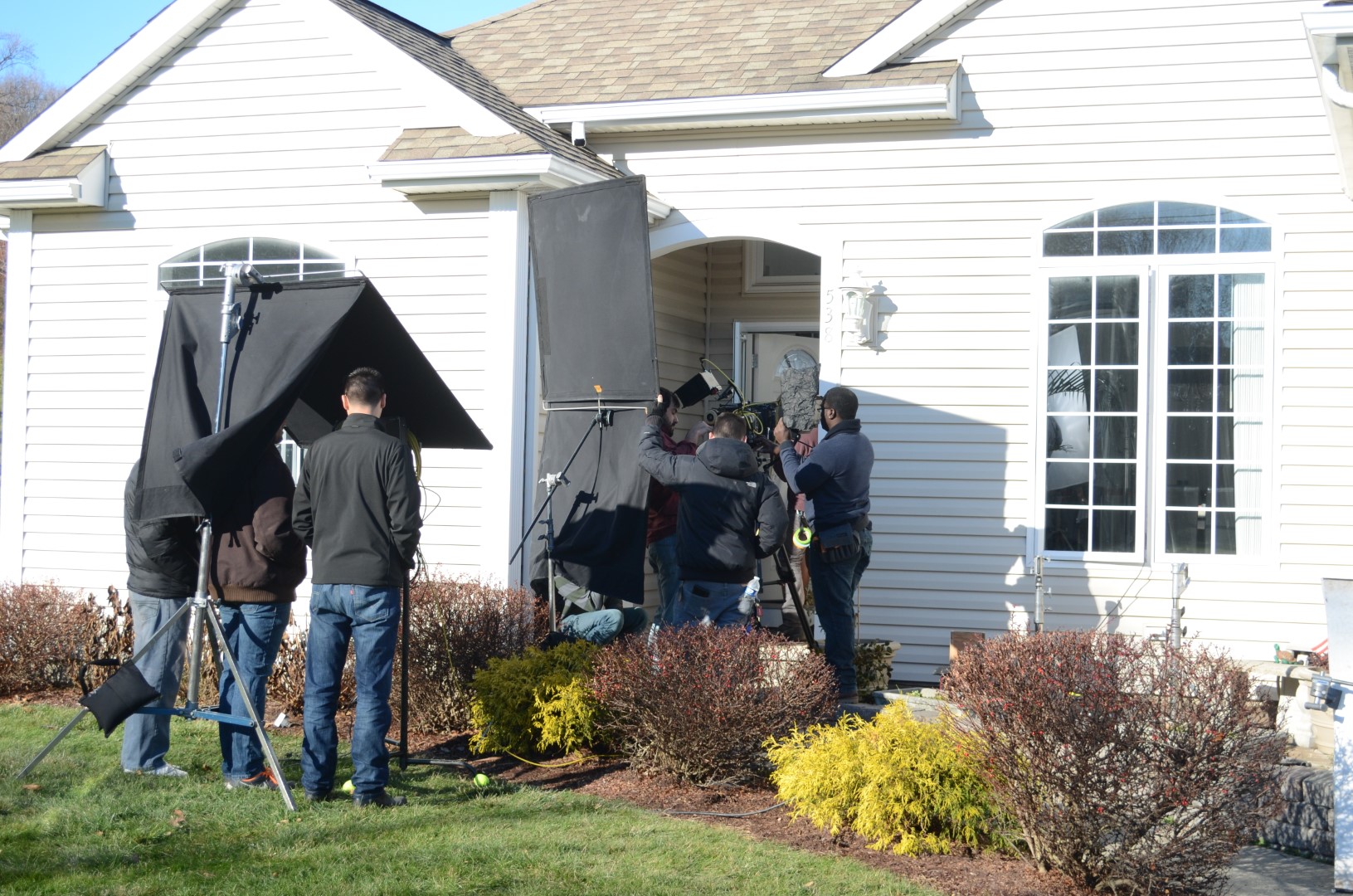 Film crew setting up equipment outside a house for a shooting scene with various filming tools.