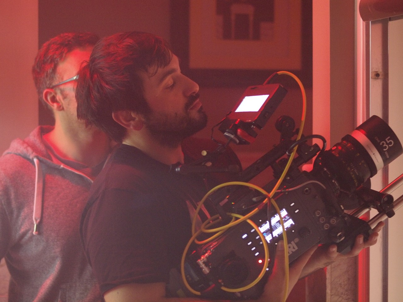 Cinematographer Vasilios Sfinarolakis focuses on camera setup in a red-lit studio during a film shoot.