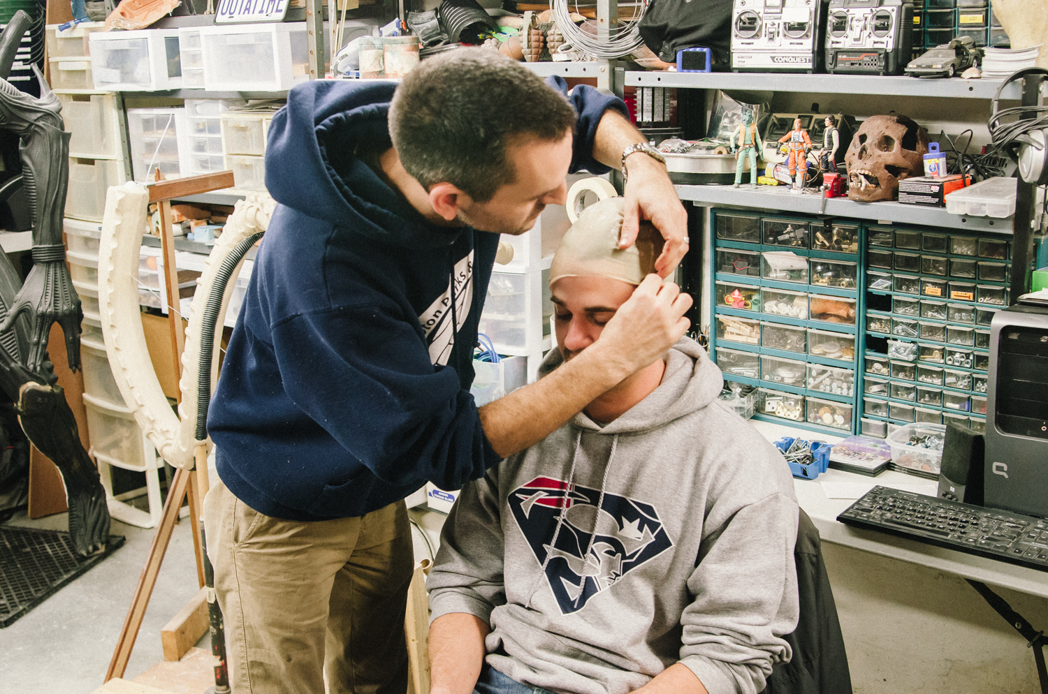 Two men in a workshop working on special effects makeup and prosthetics with various tools around them.
