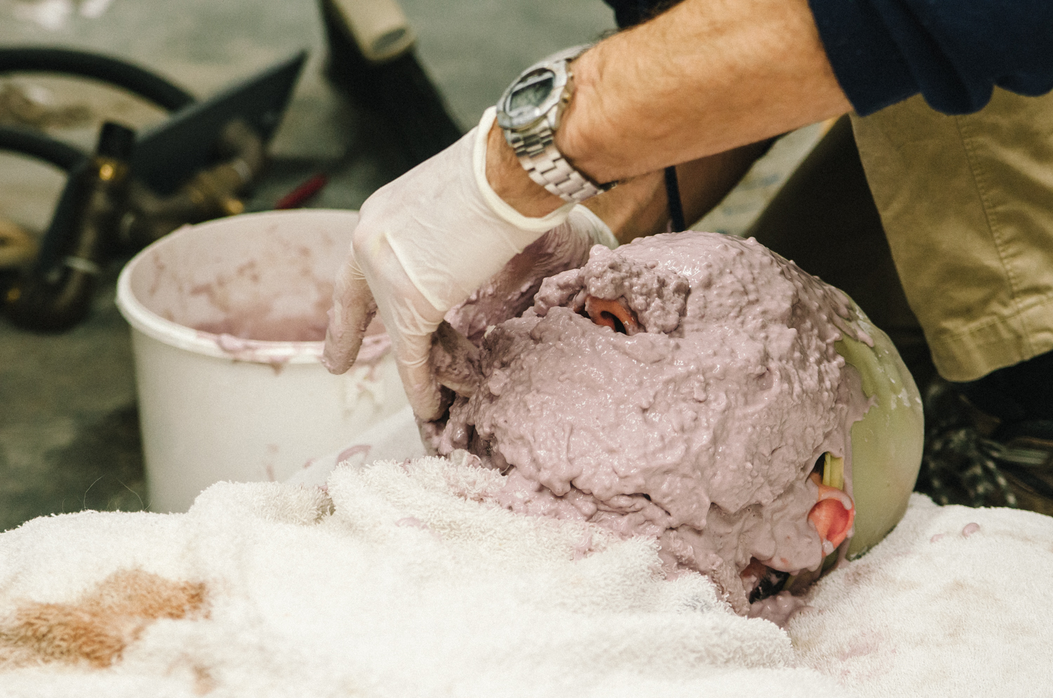 A person applying a thick, purple mold to a head form, with supplies nearby.