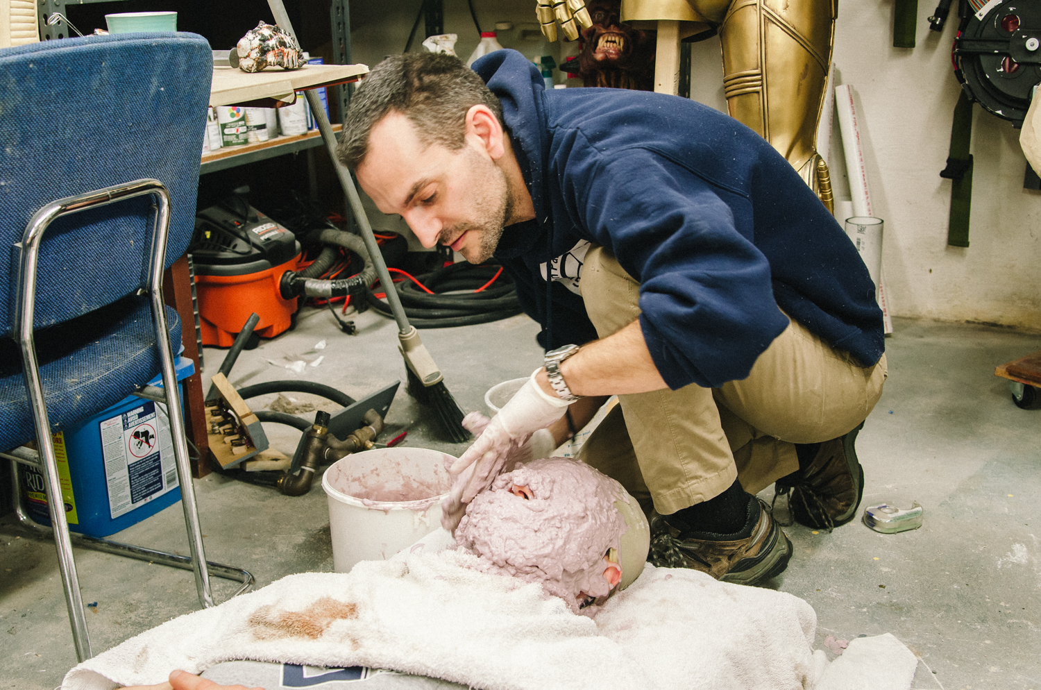A man molds a pink casting material over a head model in a creative workshop.