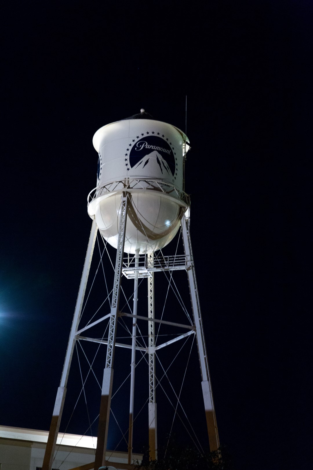 Illuminated water tower at night, featuring the Paramount logo on its white structure.