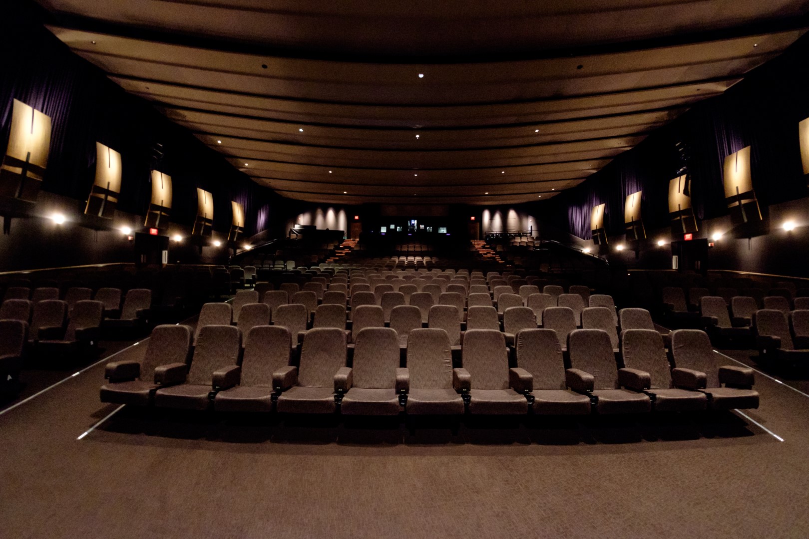 Interior view of a spacious cinema hall with empty rows of cozy seating and soft lighting.