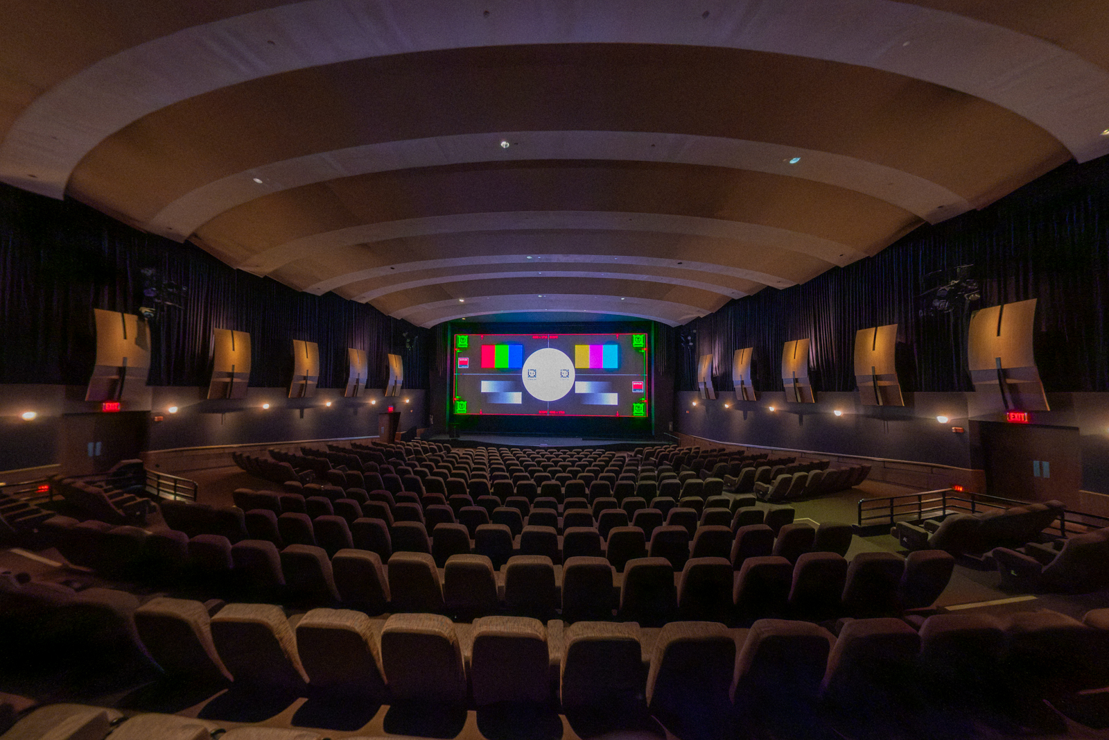 Interior of a movie theater with empty seats and a large screen displaying test patterns.