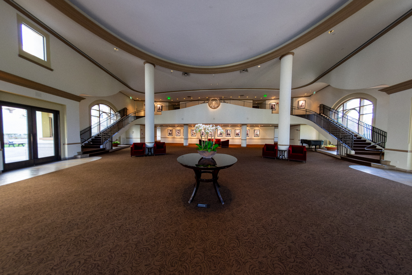 Elegant lobby featuring a central table, plush seating, and grand staircase with framed artwork.