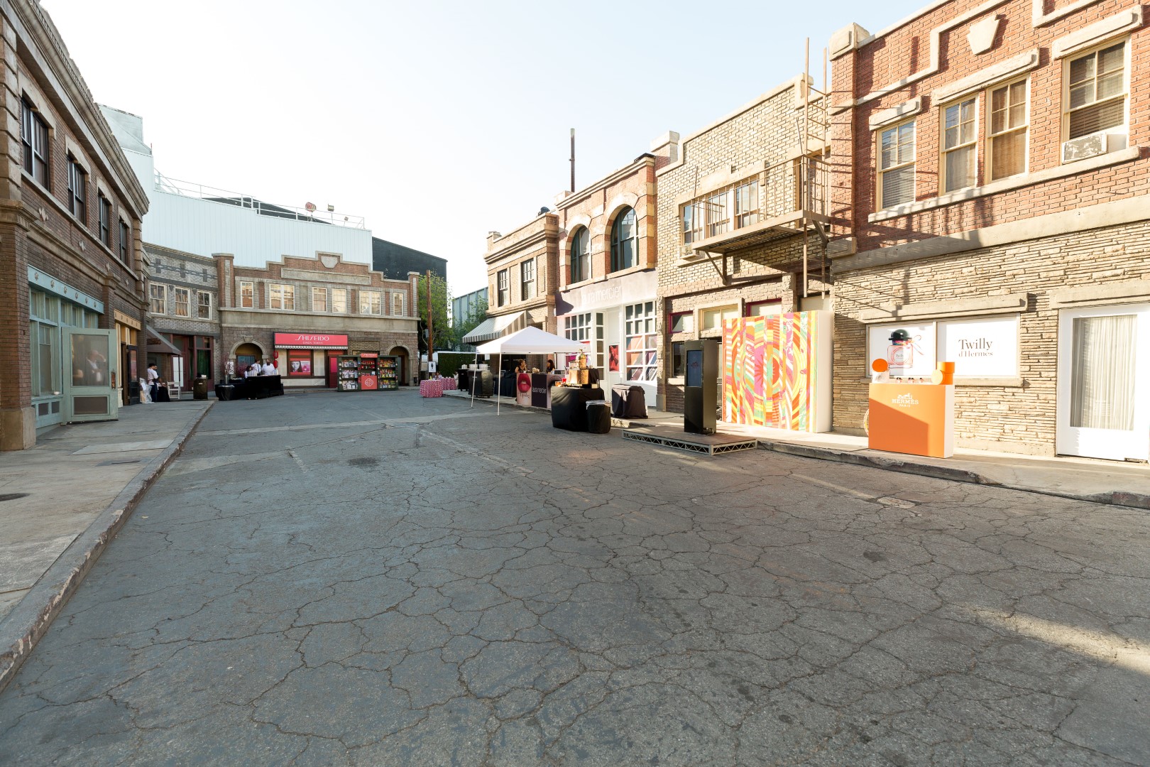 Empty urban street with vintage buildings, colorful displays, and outdoor event setups in bright sunlight.