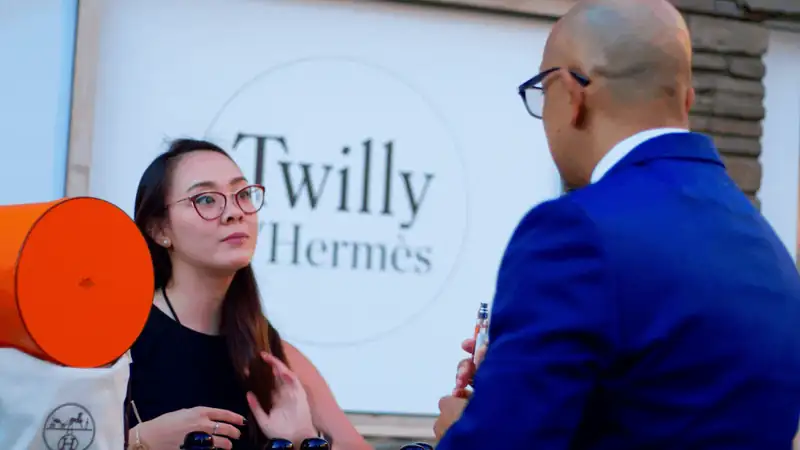 Conversation at a Twilly Hermès event featuring a woman in glasses and a man in a suit.