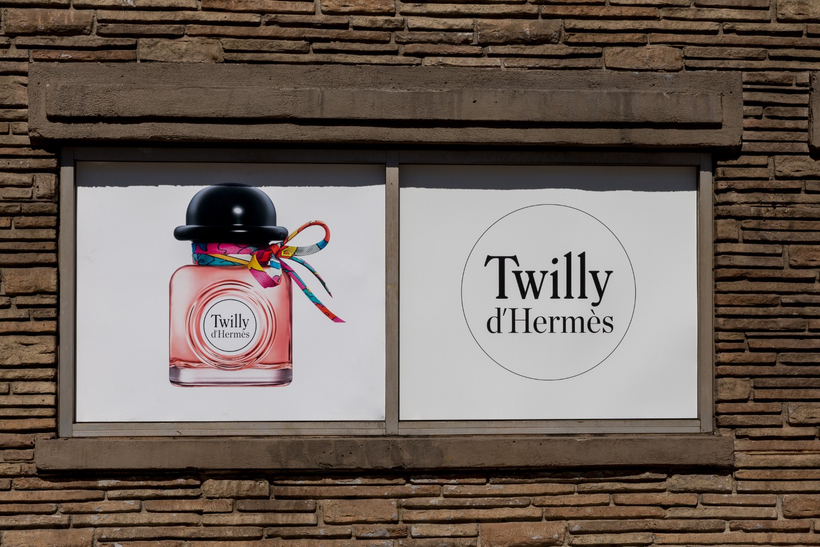 Twilly d'Hermès perfume bottle displayed on a wall with colorful ribbon accents.