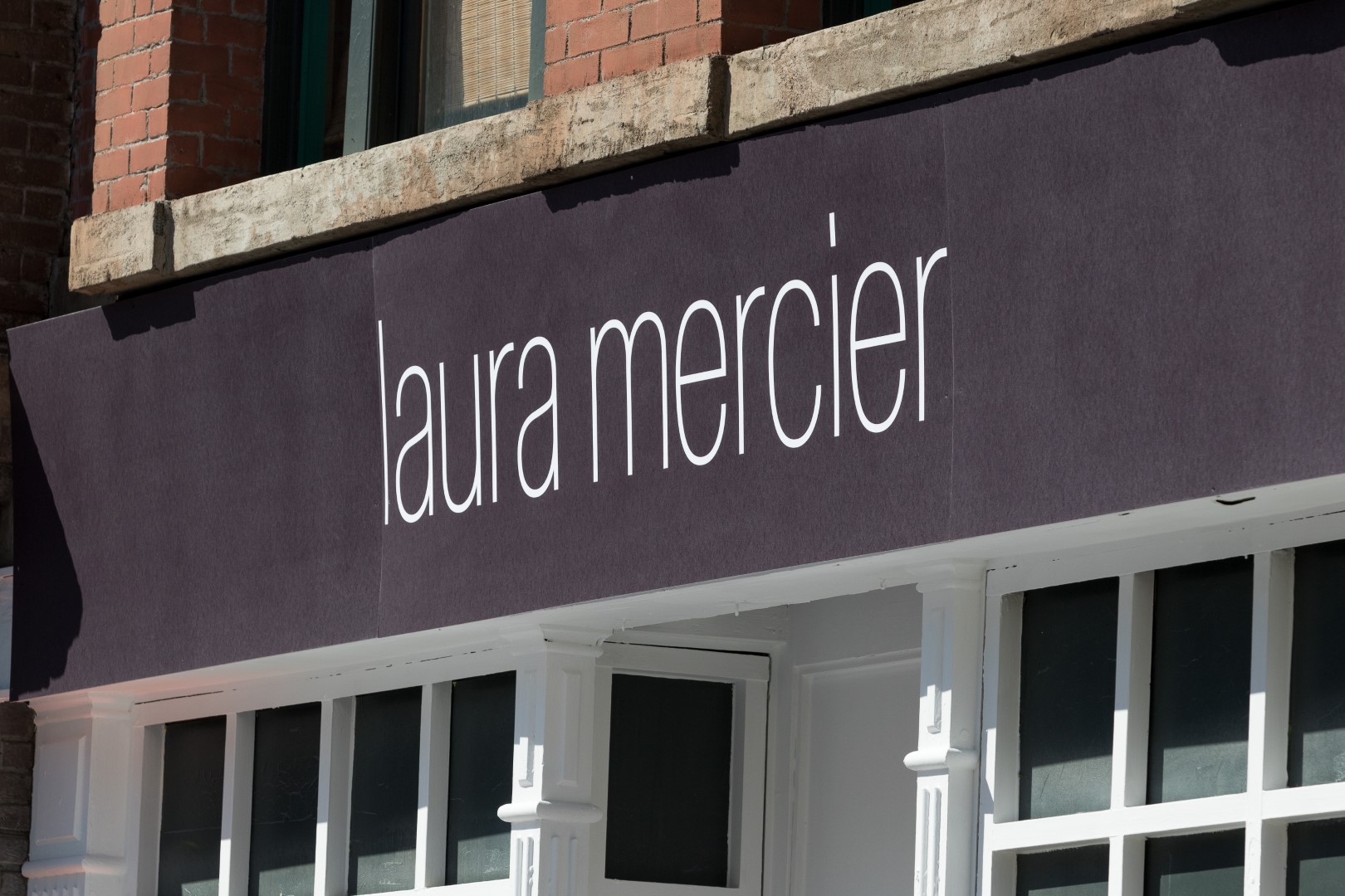 Exterior view of a Laura Mercier store sign on a brick building.