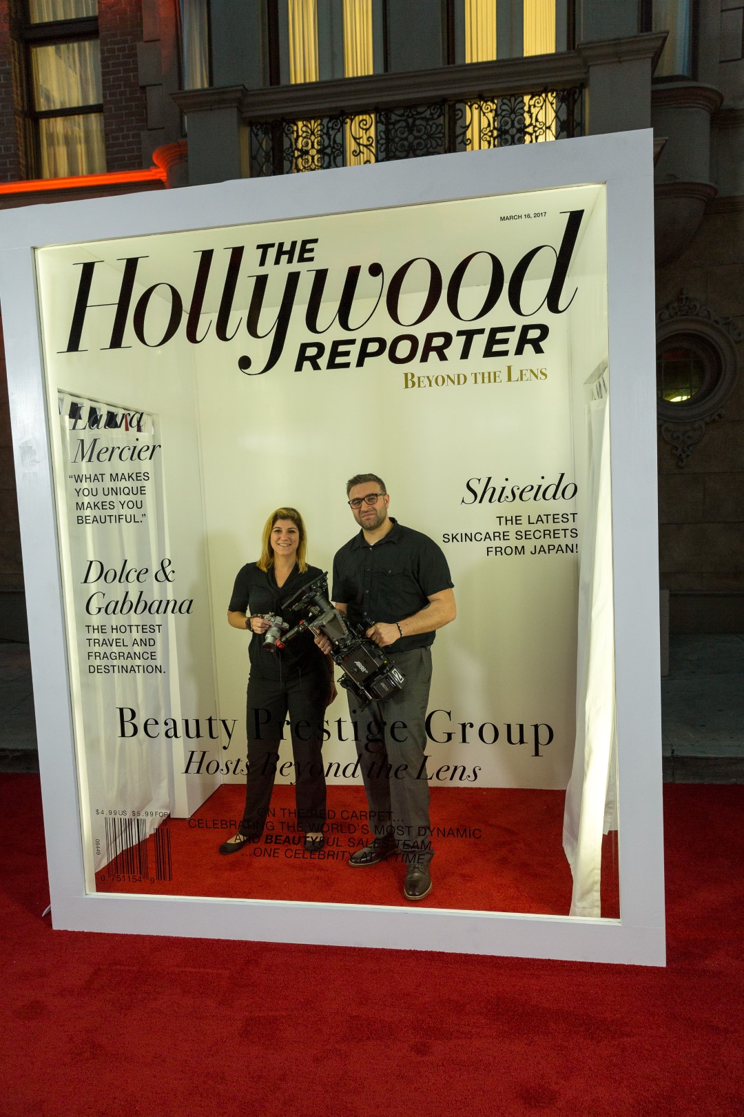 Paul Melluzzo poses with a camera next to Trish Fearon at a beauty event on a red carpet.