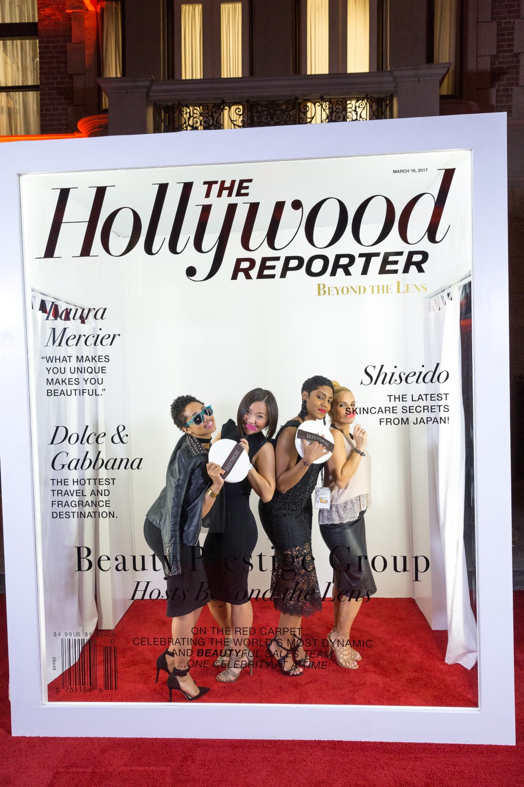 Models pose in a Hollywood Reporter cover frame at a beauty event on the red carpet.