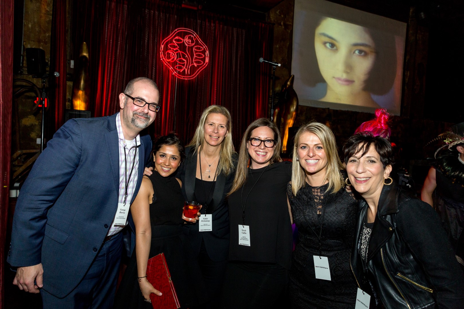Group of six smiling guests at an event, with a stylish backdrop and a projection in the background.