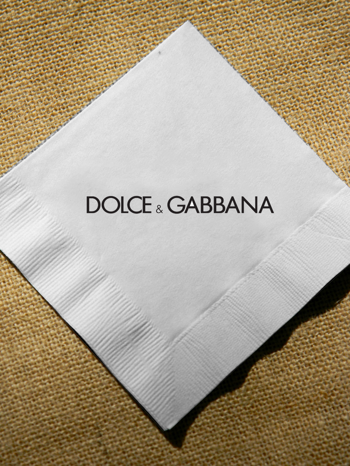 Dolce & Gabbana logo on a white napkin against a textured background.