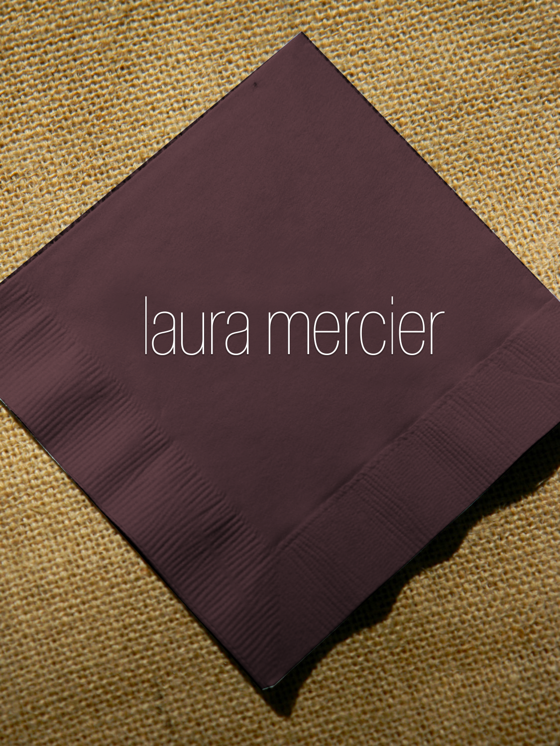 Laura Mercier logo on a dark napkin over a textured background.
