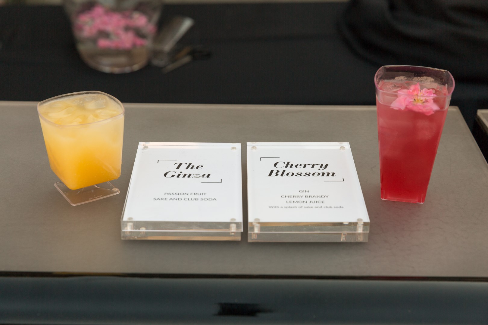 Cocktails 'The Ginza' and 'Cherry Blossom' with drinks and detailed menus on a bar counter.