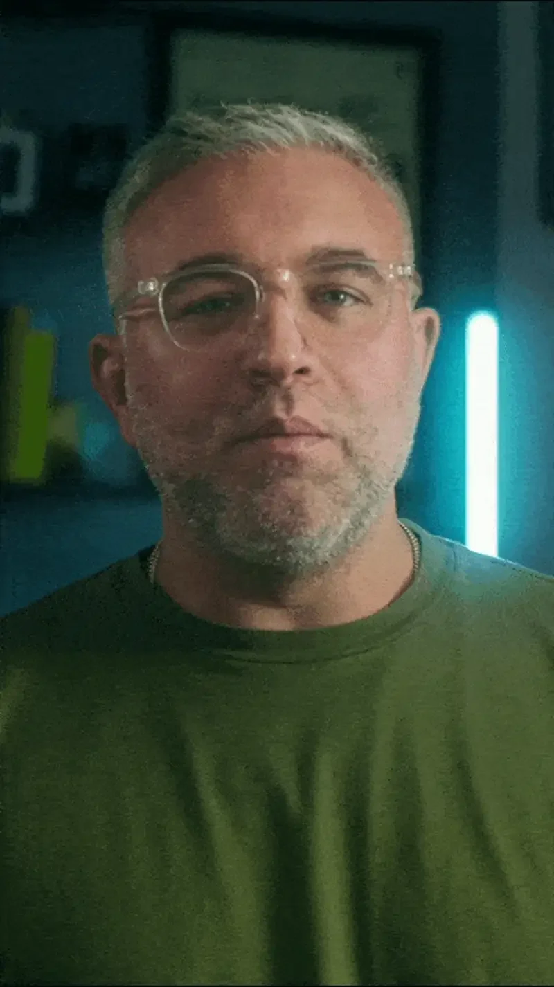 Confident man with glasses in a green shirt, illuminated by a blue light in a modern setting.