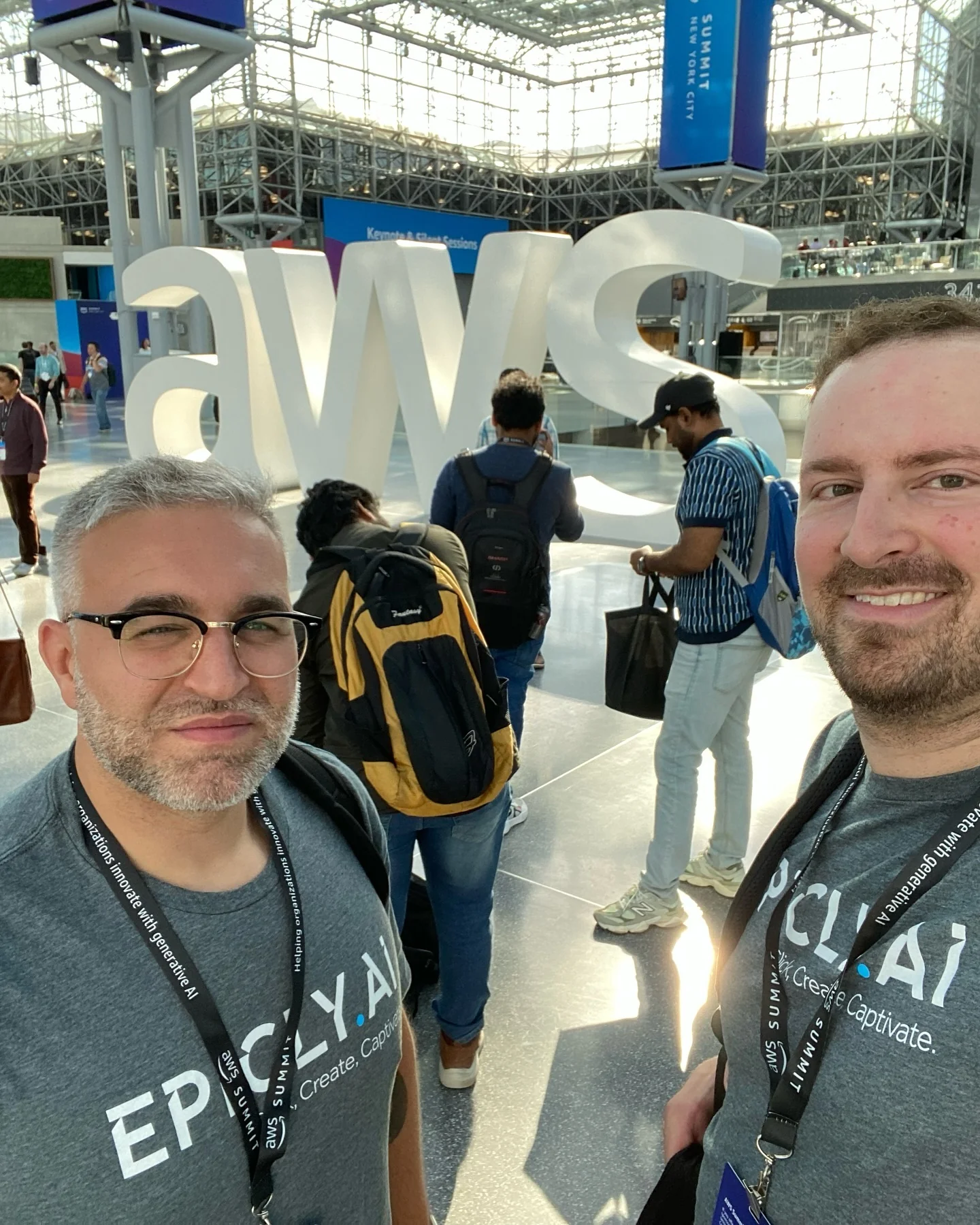 Paul Melluzzo and Torrey Benane in gray shirts with 'EPICLY.AI' logo at AWS event location.