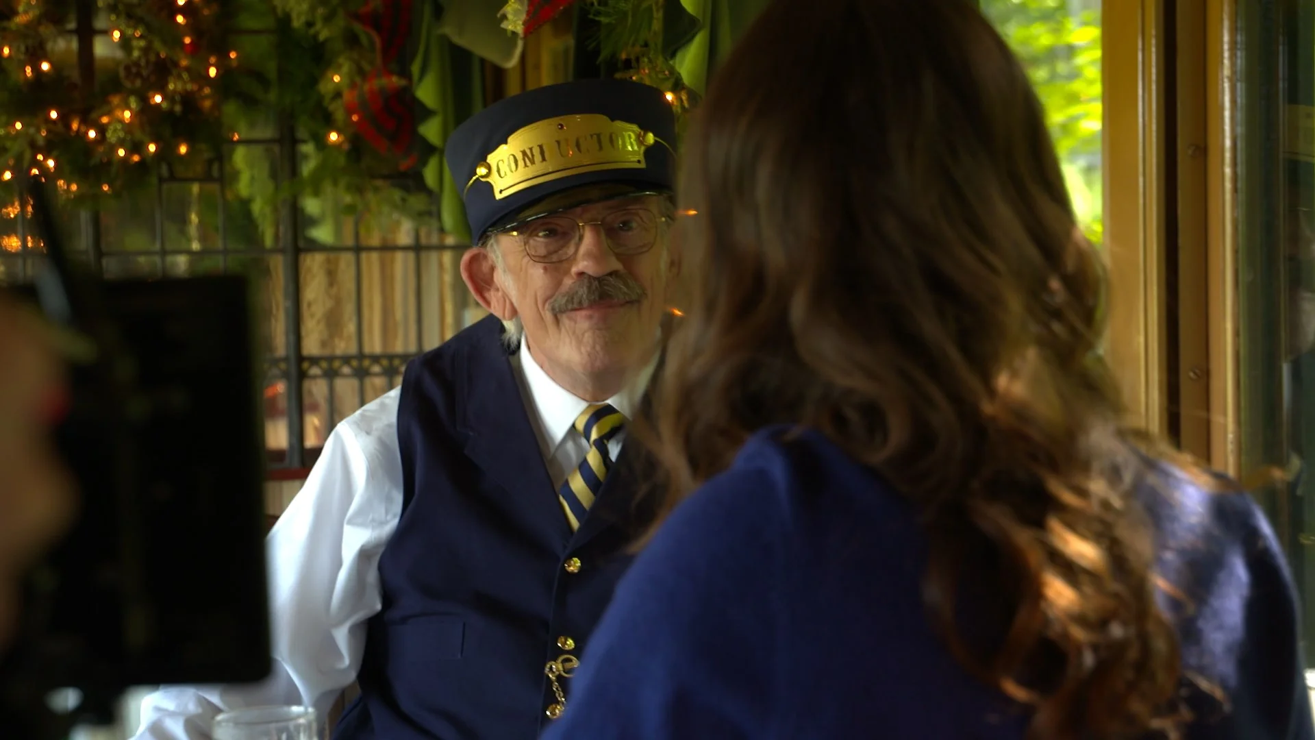 Christopher Lloyd as a train conductor chatting with a woman in a decorated train car.