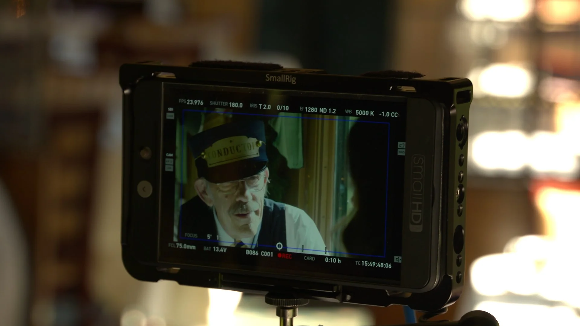 Close-up of a camera monitor showing an actor in a conductor's hat during a film scene.