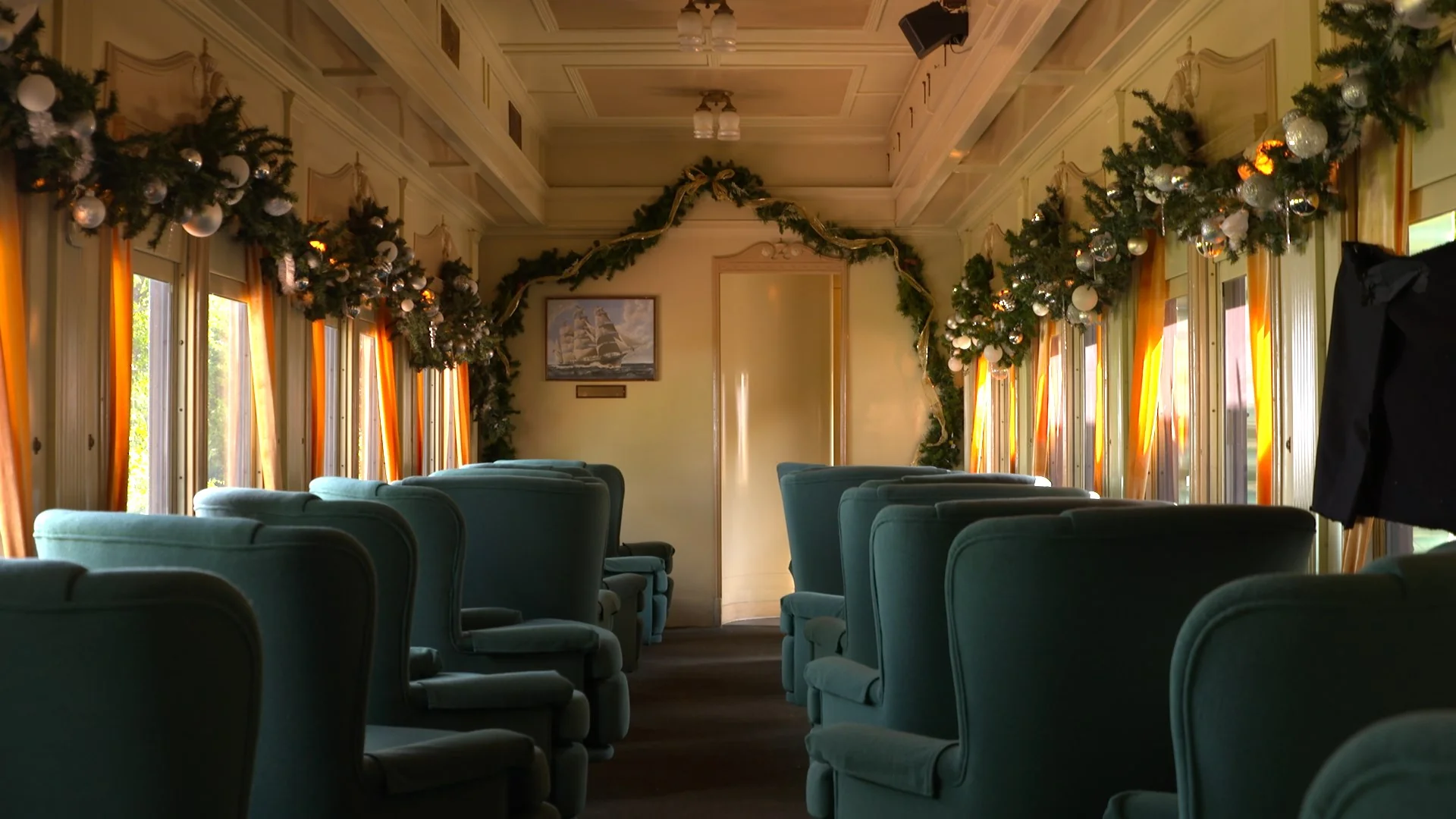 Interior of a train car decorated for the holidays with green chairs and garlands.