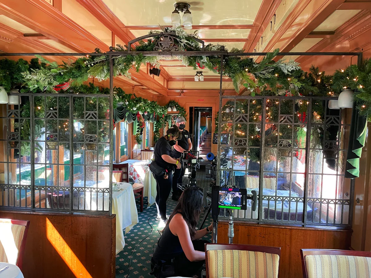 Interior of a train car decorated for the holidays with filming crew and equipment.