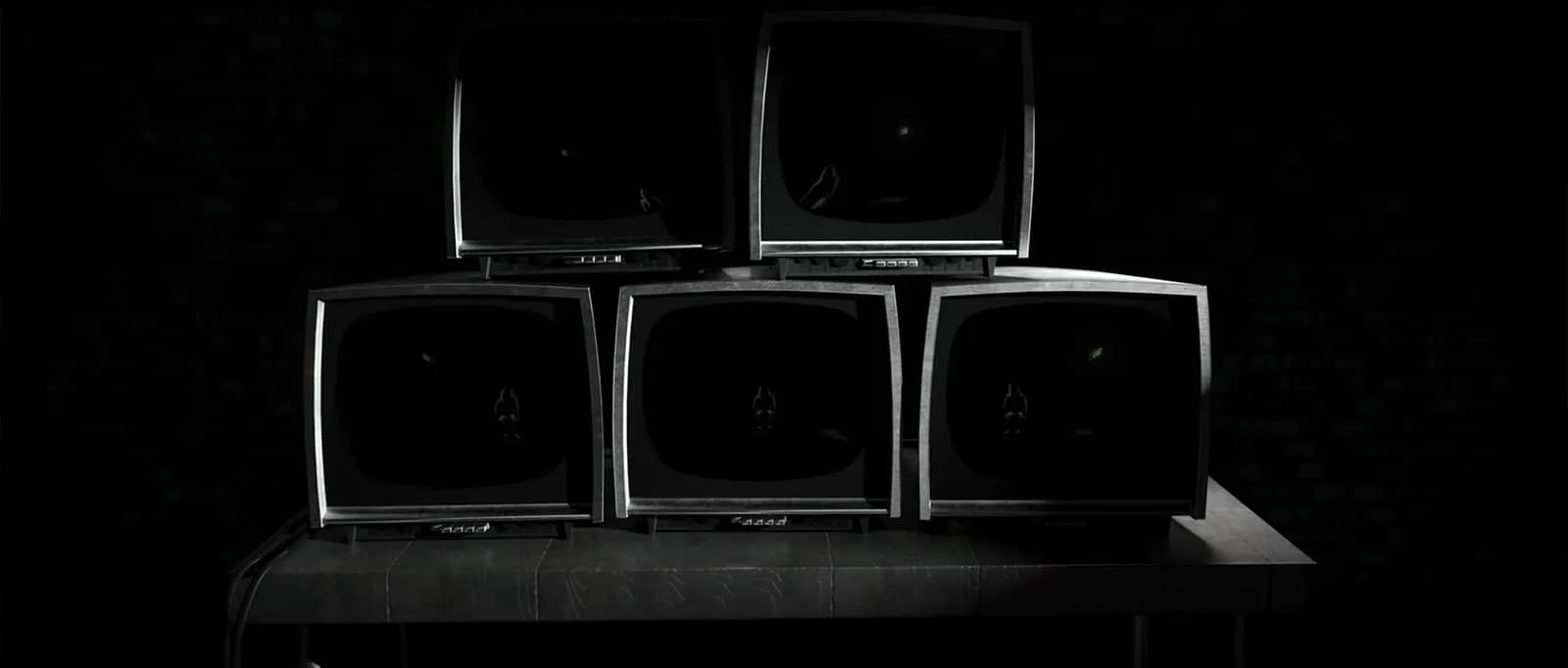 Five vintage TVs stacked on a dark table in a dimly lit environment.
