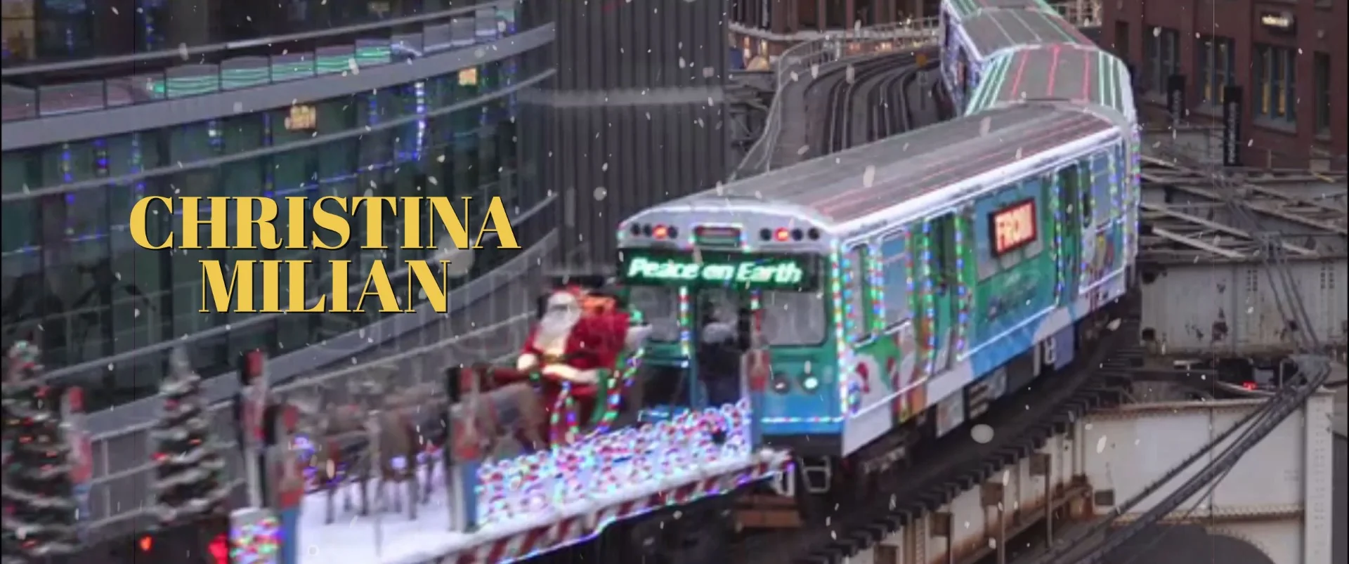 Colorful train with holiday decorations and Santa riding on top during snowfall.