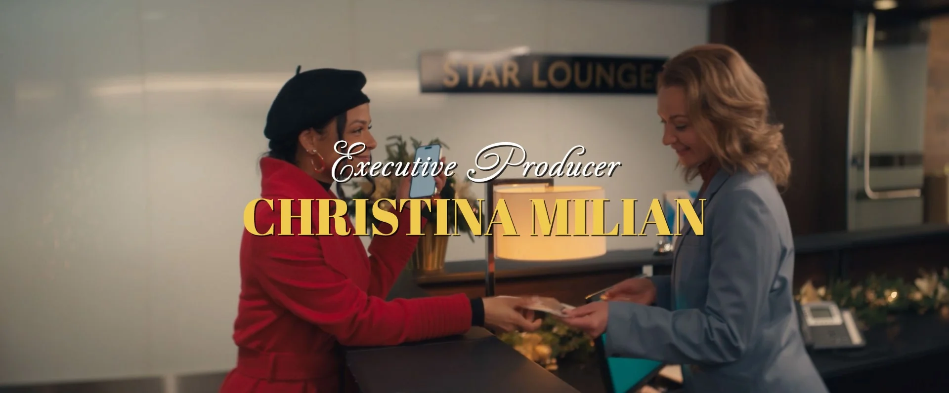 A woman in a red coat hands a ticket to another woman at the reception desk.