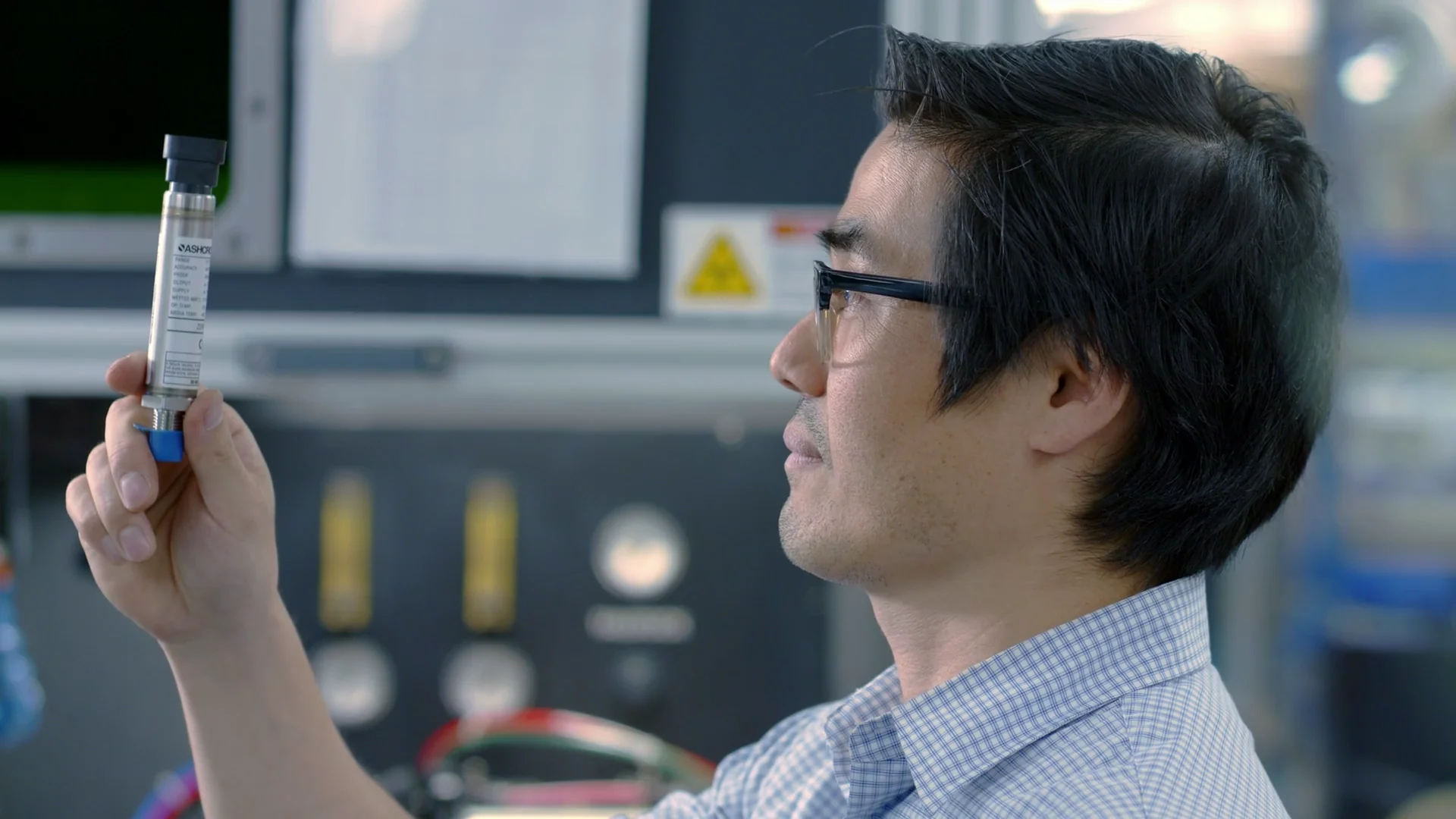 A man examines a pressure transducer with a blue cap and label in a lab setting.