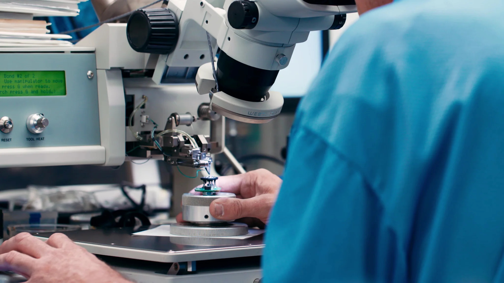 Technician using a microscope for precise work on a component in a lab setting.