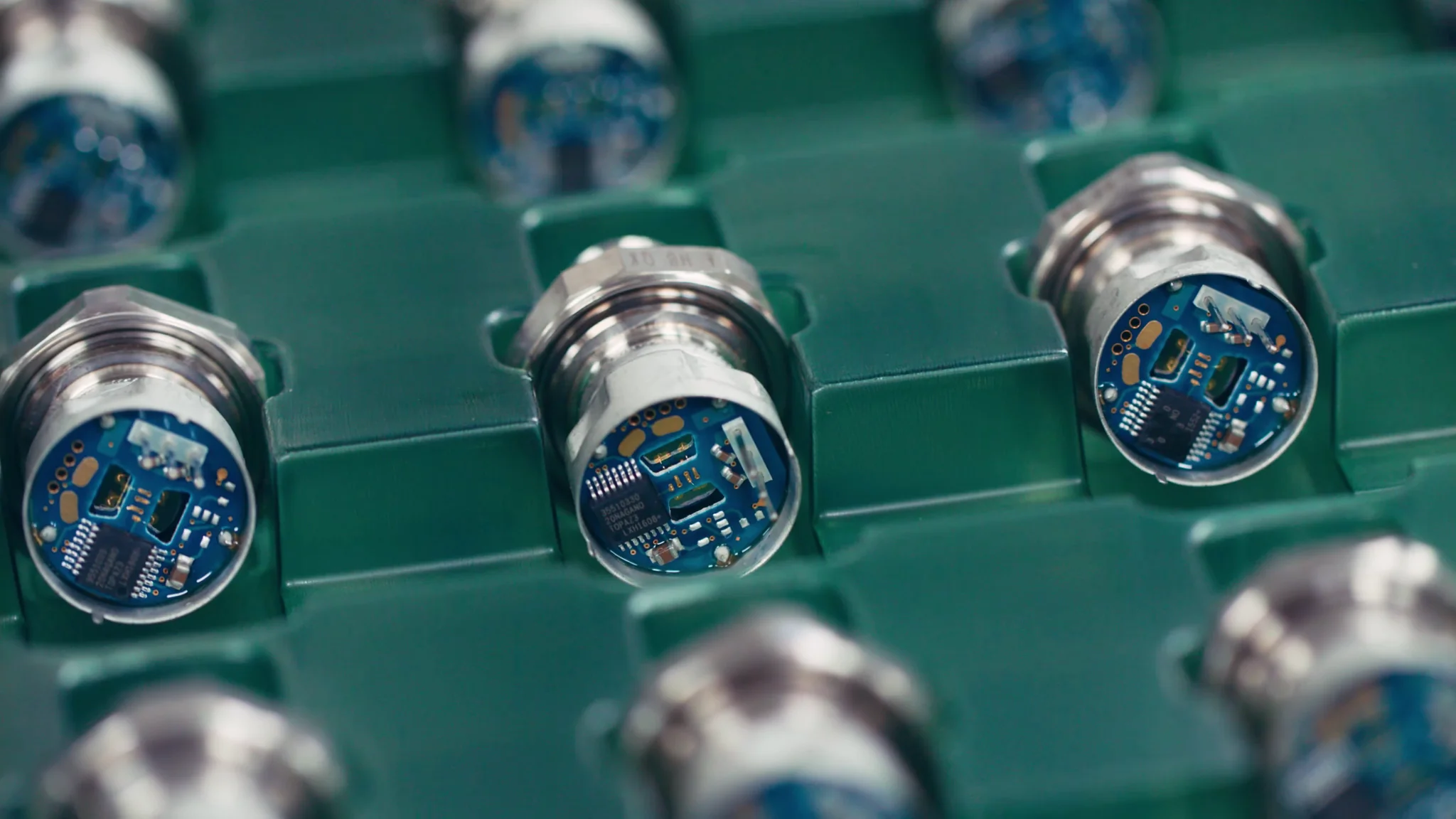 Close-up of electronic components with blue circuit boards in green trays, showcasing manufacturing precision.