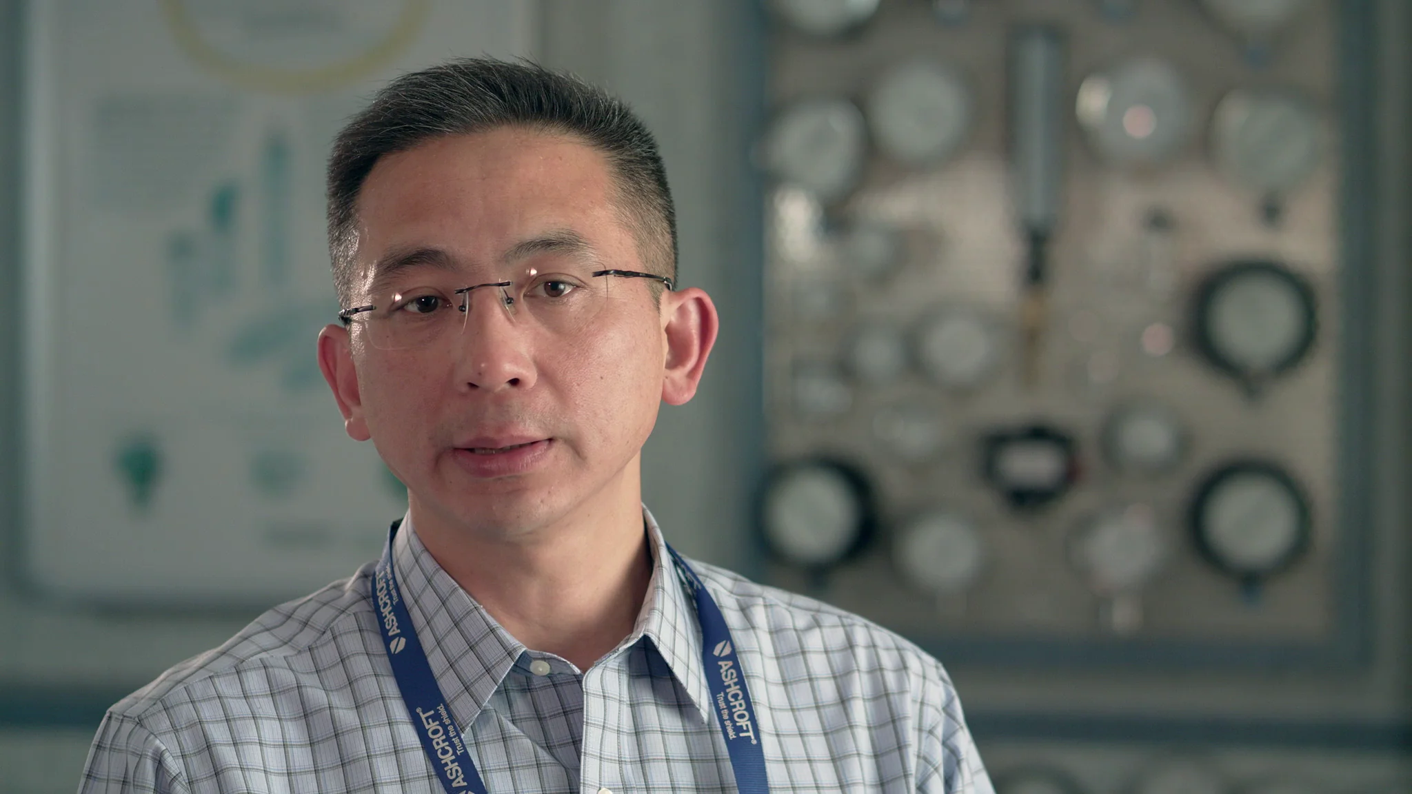Professional man in a checked shirt speaking in front of a backdrop of gauges and instruments.