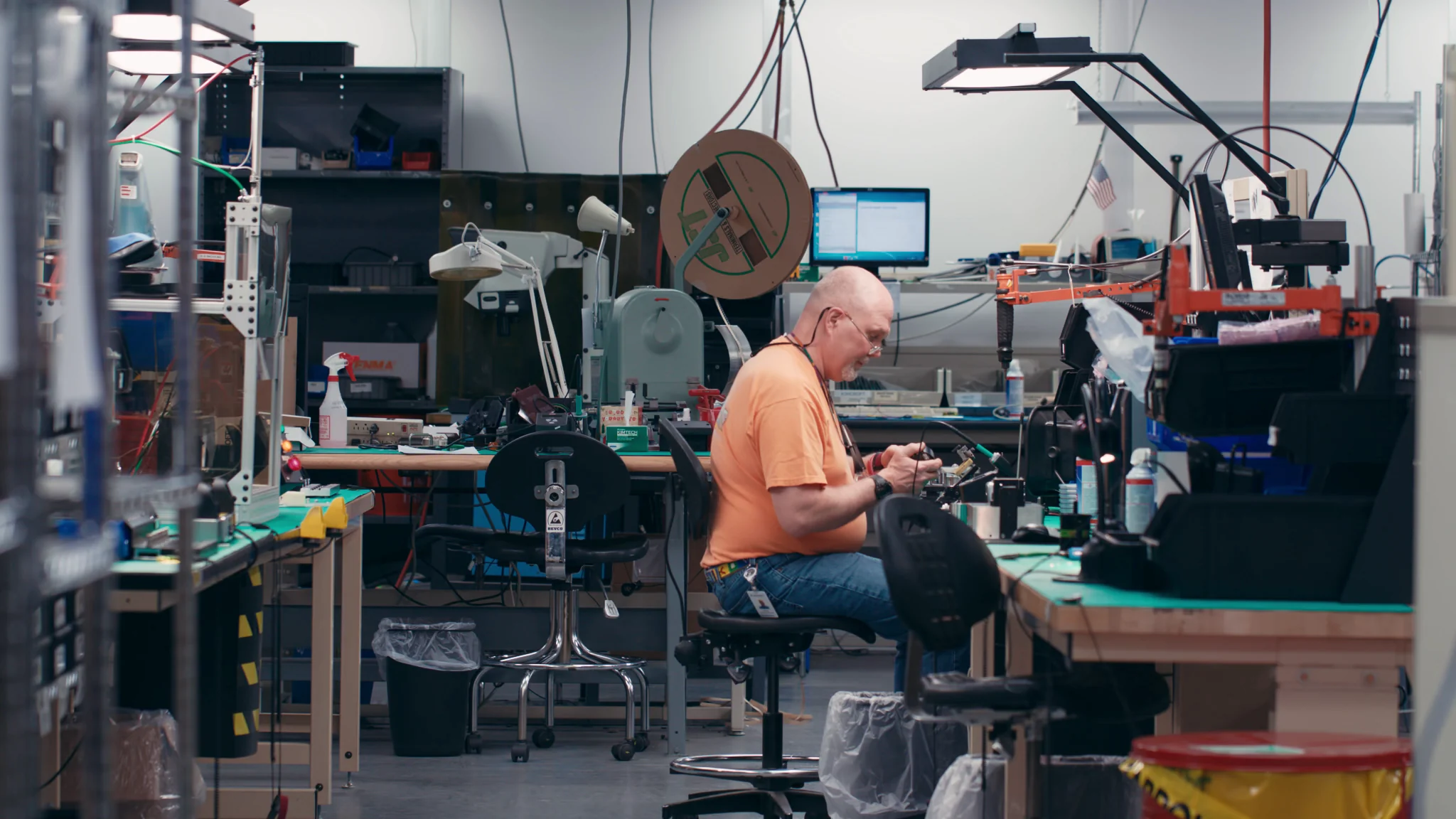 Person working in a high-tech electronics lab, surrounded by tools and equipment.