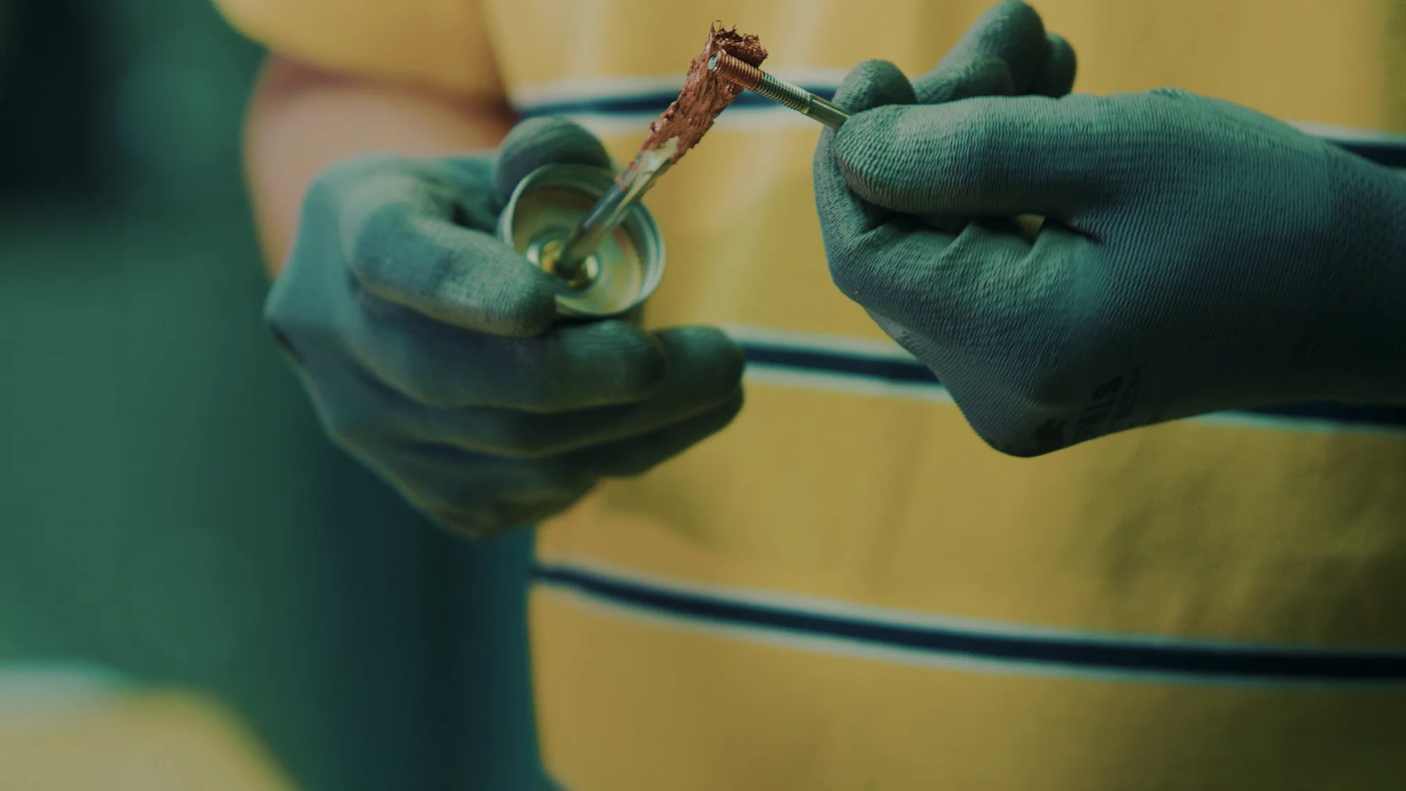 Person in gloves holding a tube and applying a brown paste, showcasing hands-on work.