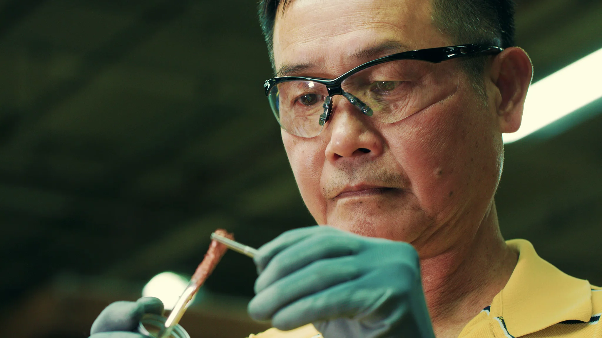 Scientist examining a specimen with precision tools and wearing safety glasses and gloves in a lab setting.