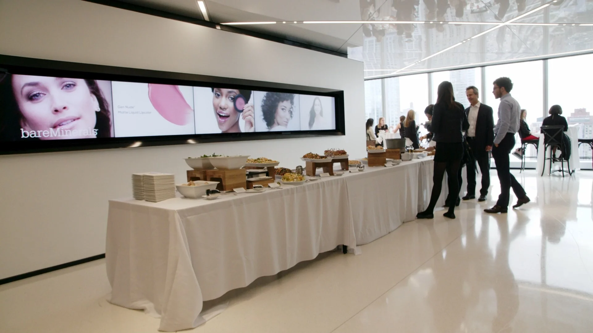 Event featuring a buffet with various food items and a large screen displaying beauty products.