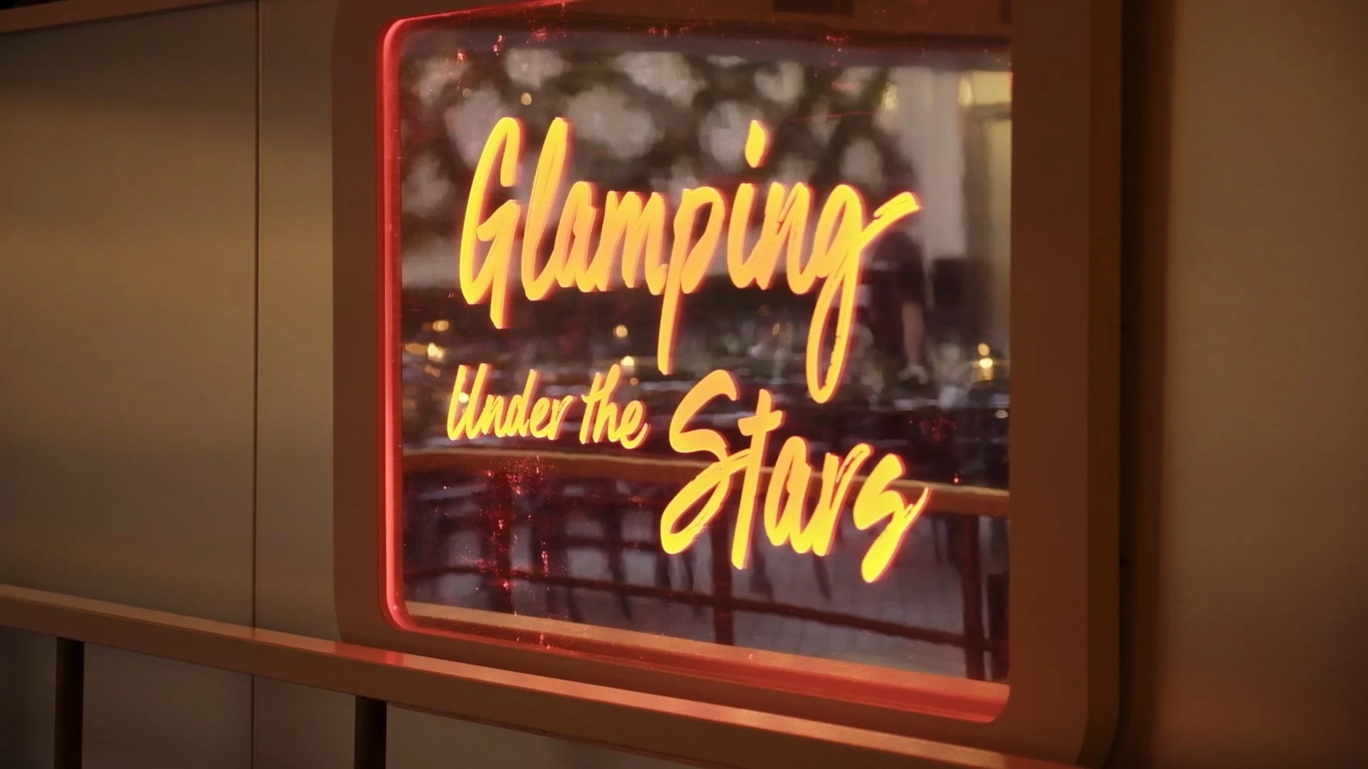 Neon sign reading 'Glamping under the Stars' in warm colors.
