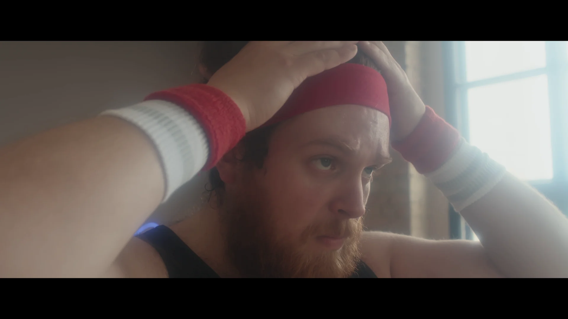 Focused man adjusting red headband while preparing for a workout in a bright gym studio.